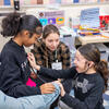 One girl practicing using a stethoscope on another girl while a third girl watches.